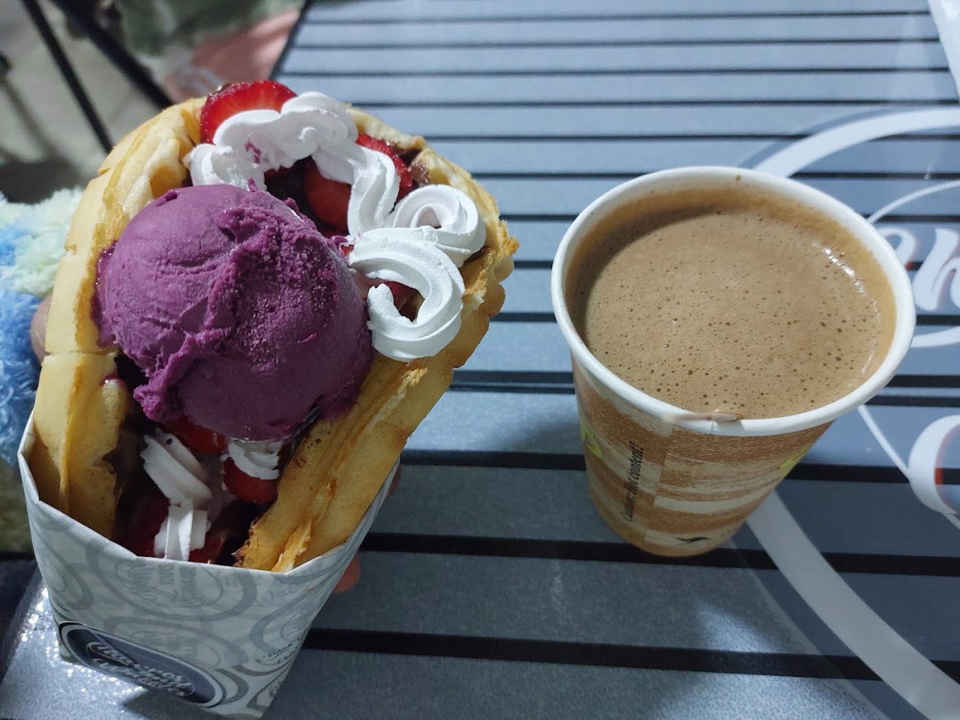 Waffle de Churros and Waffles en su envoltorio de marca, con helado de berries, frutillas, chocolate y crema, junto a un café